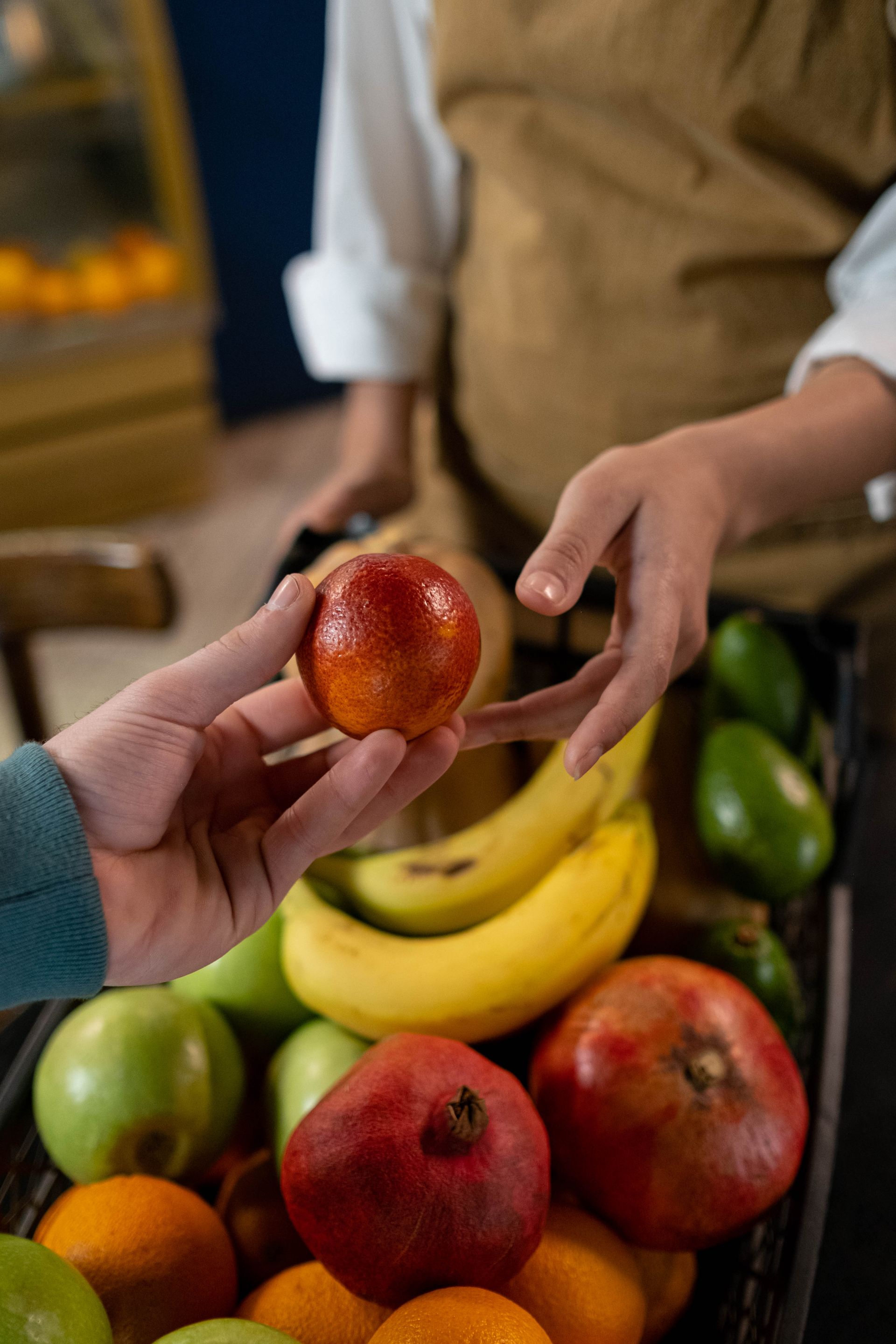 Two hands passing a blood orange across a crate of fruit